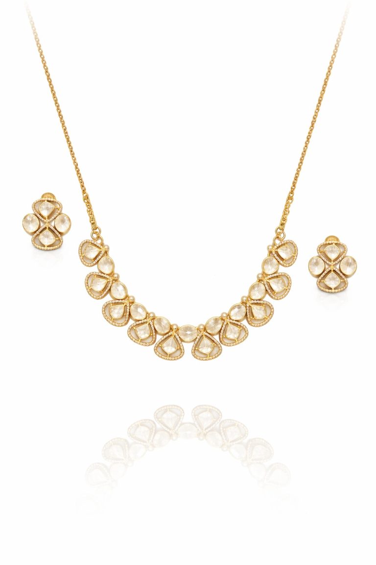 Gold-plated statement necklace set with matching stud earrings, featuring pear-shaped and oval crystal stones arranged in a cascading design, photographed on a white background with the necklace appearing to hang in the air and a soft reflection below