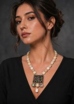 Woman wearing vintage Egyptian pendant necklace with natural stone beads and matching square drop earrings, styled with black V-neck outfit, close-up view of elegant statement jewelry.